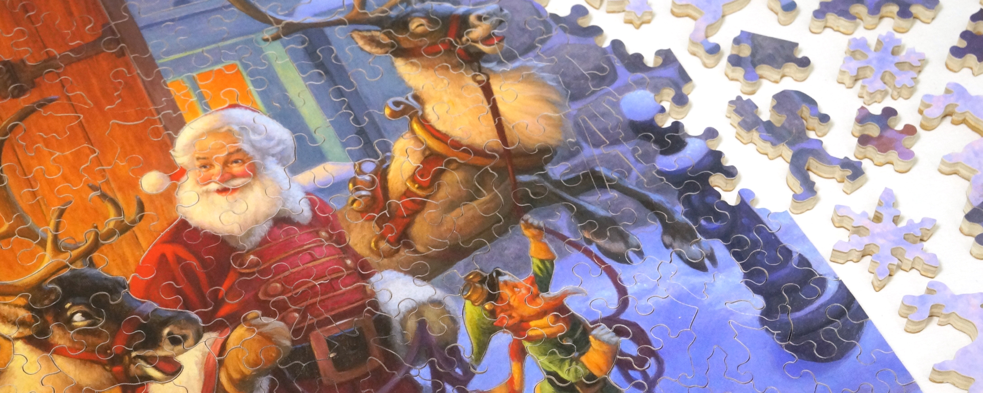 Wooden Christmas jigsaw puzzle featuring Santa Claus, his elf, and his reindeer as well as puzzle pieces in classic Christmas shapes such as elves holding gifts, snowflakes, and reindeer.